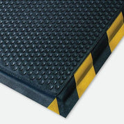 A close-up of a anti-fatigue mat black textured rubber mat with yellow and black striped corner guards, shown on a light gray background.