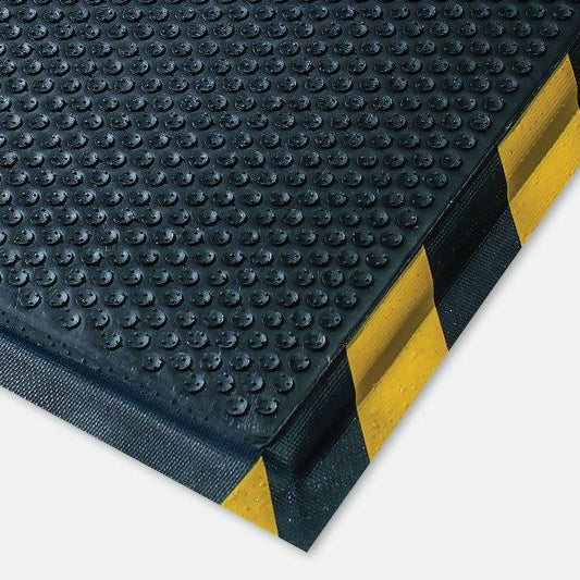 A close-up of a anti-fatigue mat black textured rubber mat with yellow and black striped corner guards, shown on a light gray background.