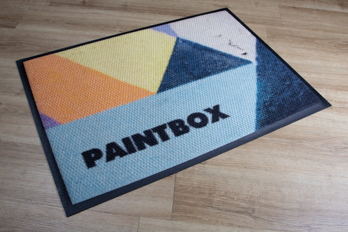 Geometric patterned mat with 'PAINTBOX' branding on a wooden floor.