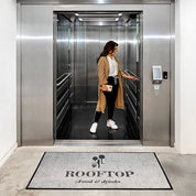 Woman entering an elevator with a 'Rooftop Food & Drinks' mat in the foreground.