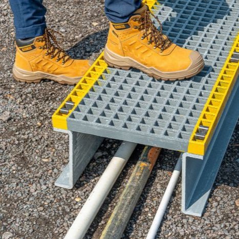 Person wearing yellow work boots stepping onto a GRP mesh grey and yellow platform on a concrete surface.