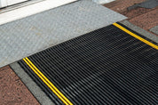 Transition strip between a textured gray mat and a black mat with yellow stripes on a textured surface.