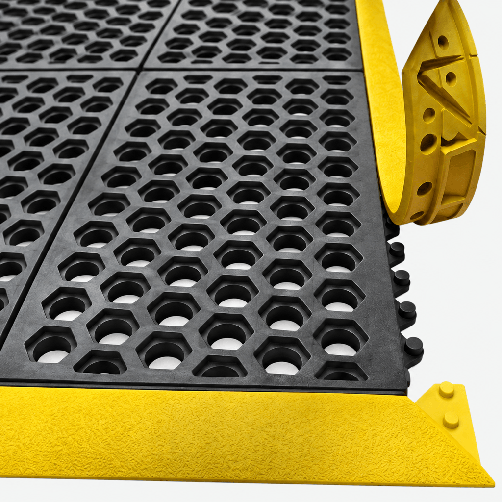 Close-up of a black rubber anti-slip grid mat with a bright yellow metal edge and corner protectors, shown on a light gray background.