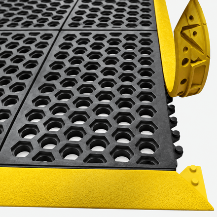 Close-up of a black rubber anti-slip grid mat with a bright yellow metal edge and corner protectors, shown on a light gray background.