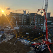 Construction site with cranes and buildings in the background during sunset.