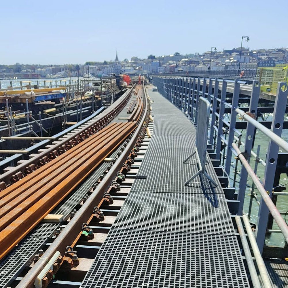 Grey GRP mesh grating on Industrial setting with metal walkways and structures, possibly a dock or warehouse.