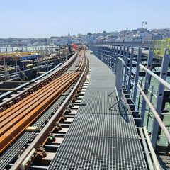 Grey GRP mesh grating on Industrial setting with metal walkways and structures, possibly a dock or warehouse.