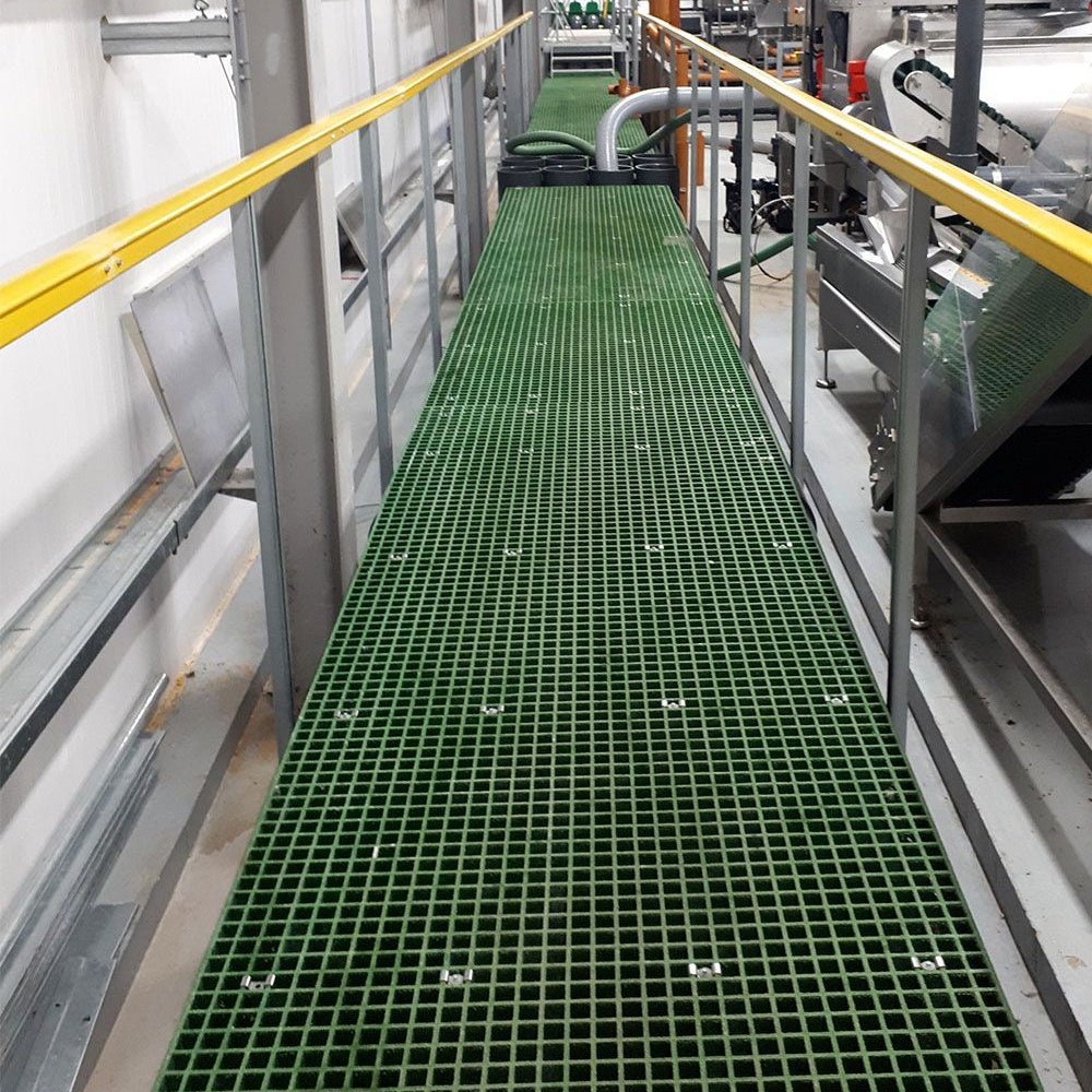 Green GRP mesh grating panels on industrial walkway with metal railings in a factory setting