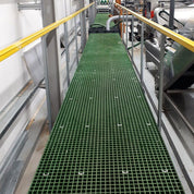 Green GRP mesh grating panels on industrial walkway with metal railings in a factory setting