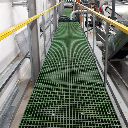 Green GRP mesh grating panels on industrial walkway with metal railings in a factory setting