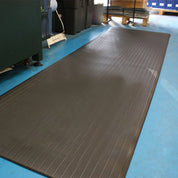A long, dark brown ribbed mat or floor cover laid out on a blue floor inside a warehouse or industrial space.
