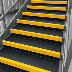 Industrial metal staircase with anti-slip black diamond-plate treads and bright yellow GRP stair nosings, clean and safety-compliant design for factories, warehouses, and commercial buildings.